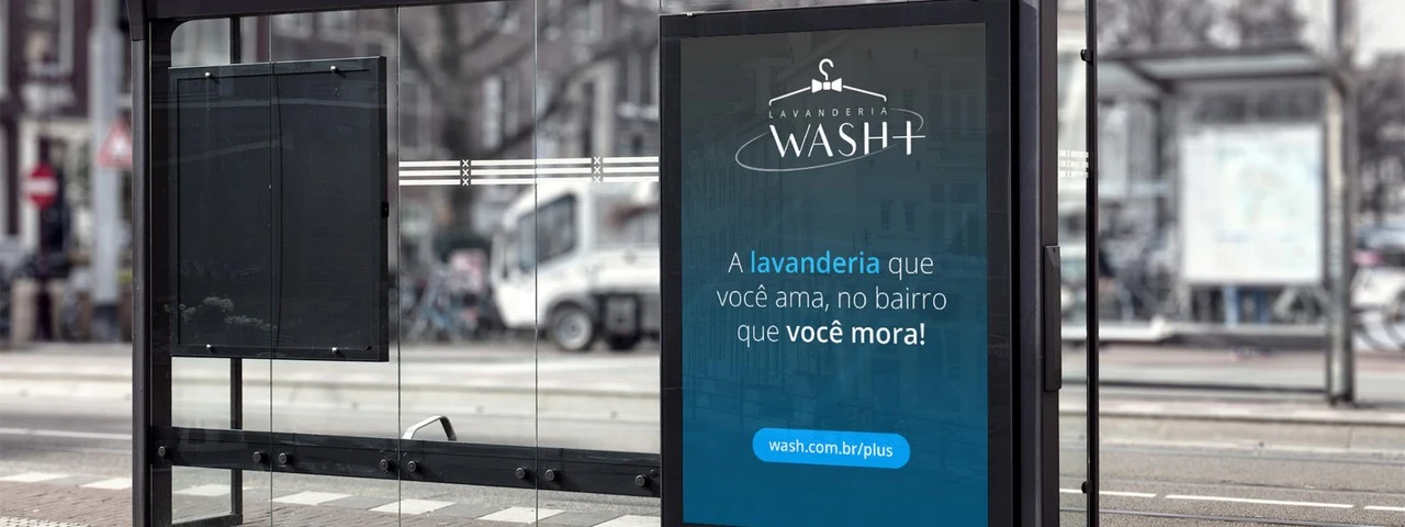 Mídia externa (ponto de ônibus) da campanha Wash+ com a assinatura "A lavanderia que você ama, no bairro que você mora!"